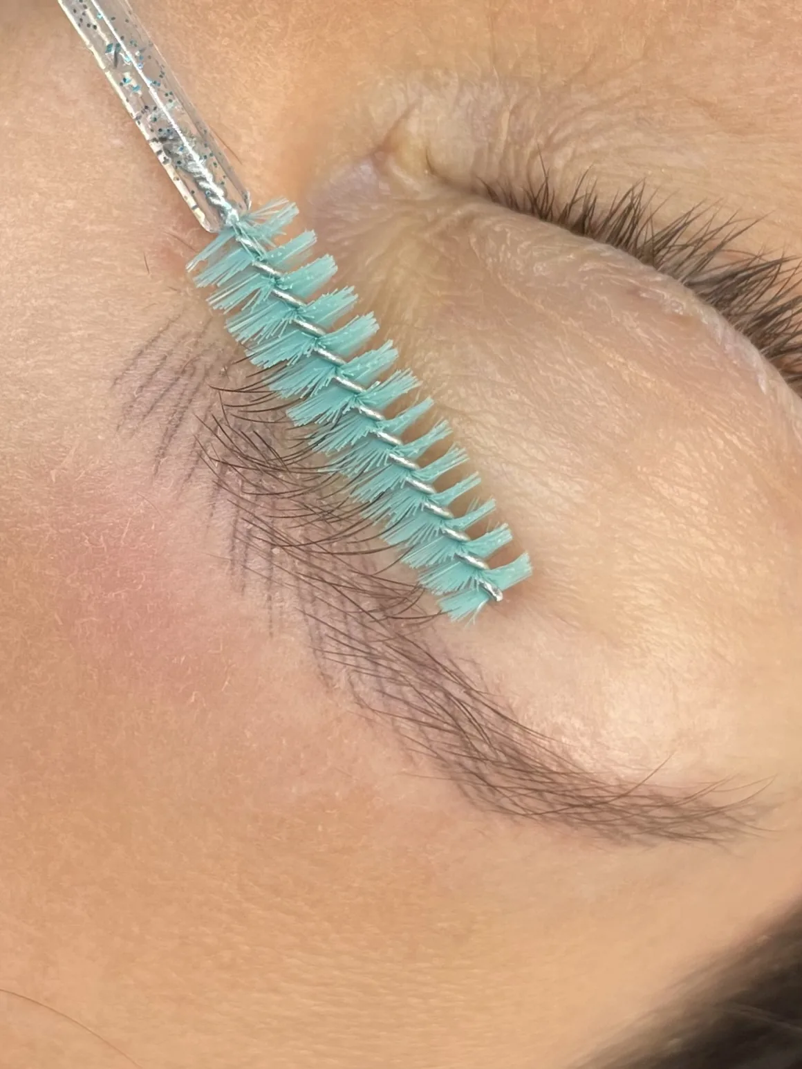 Natural brow hair brushed aside with a spoolie, revealing healed microblading strokes across the inner brow