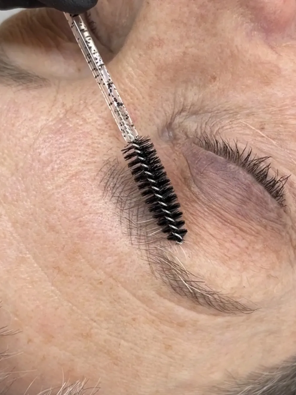 Fine healed microblading strokes running through the brow body, hair brushed aside