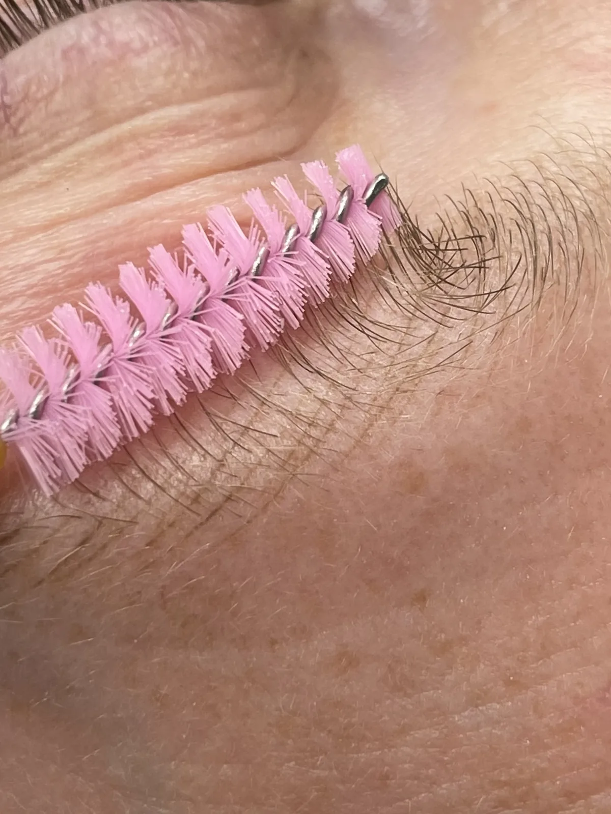 Spoolie lifting a full natural brow to show healed strokes filling the lower edge